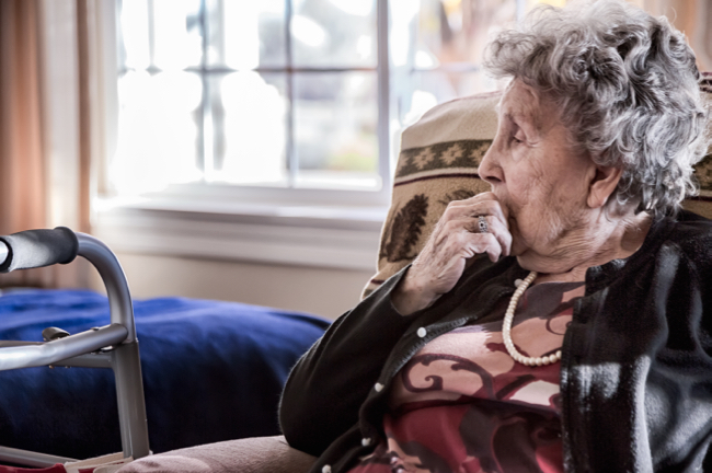 Image shows Portrait of an elderly woman sitting alone in a senior care facility.