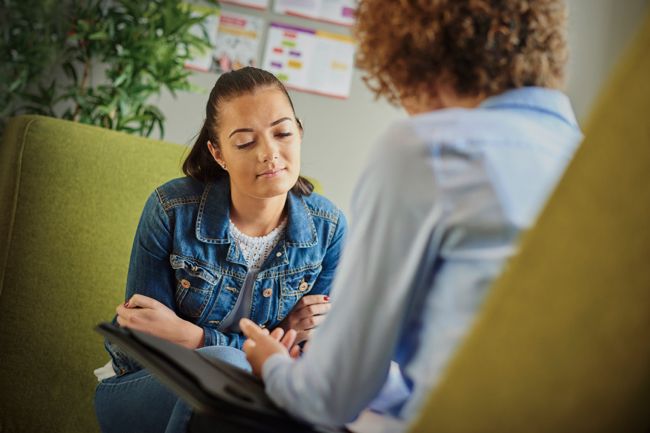 Image shows a young woman in therapy sitting opposite a counsellor and explaining her.