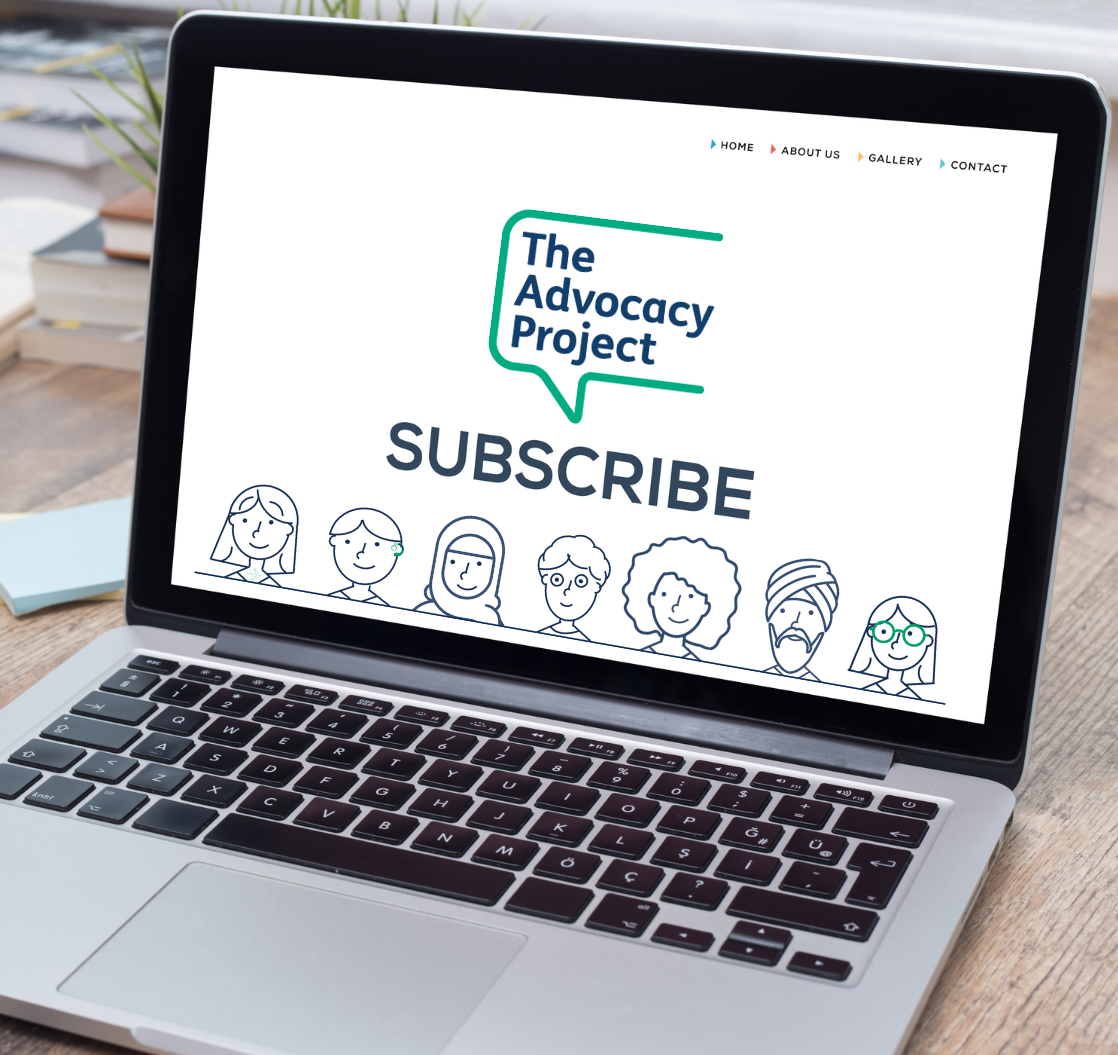 Image of an open laptop on a desk table. On the screen of the laptop is The Advocacy Project Logo, the word 'Subscribe' and along the bottom of the screen an illustration showing a diverse selection of seven heads. 